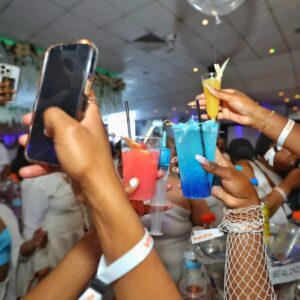 A red and blue cocktail being raised into the air with a phone capturing the moment at MUKE Life's All White Soiree